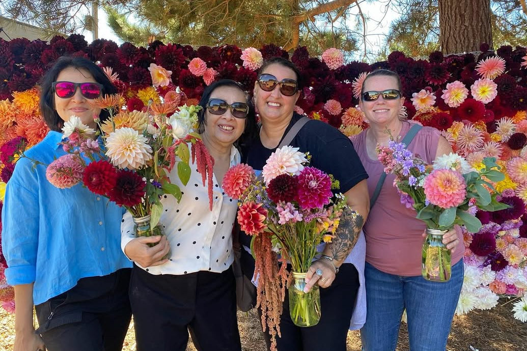 Four women holding bouquets of flowers in front of a colorful floral display.