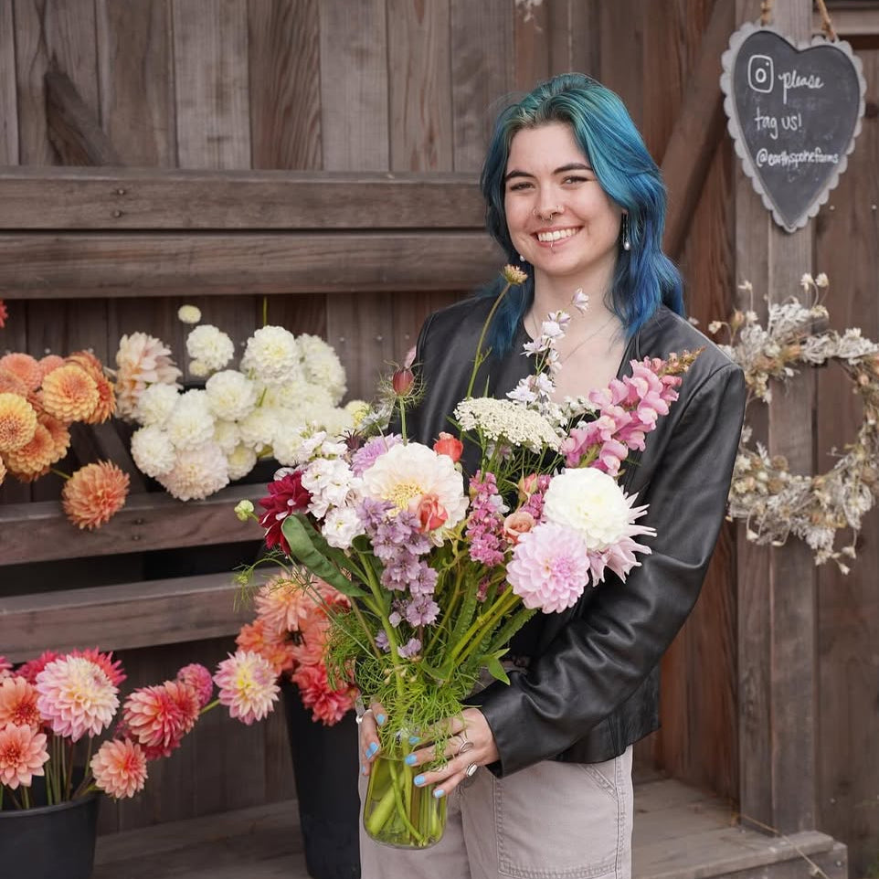 Person holding flowers in front of a wooden structure with floral arrangements.