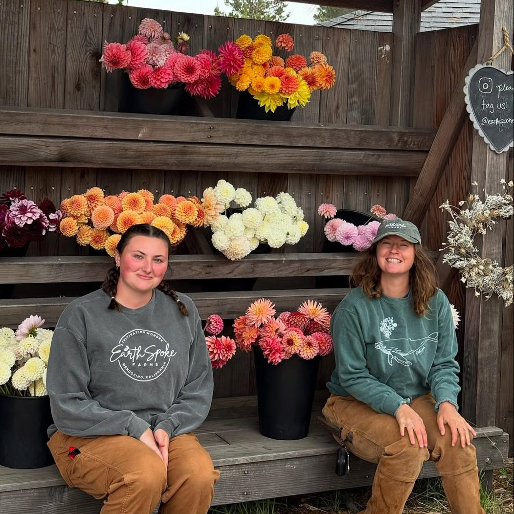 Two people sitting on a wooden bench with flower arrangements behind them.