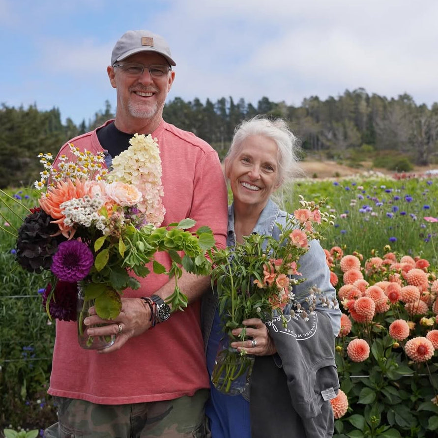 Two people holding bouquets of flowers in a field with a scenic background